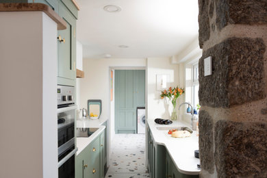 コーンウォールにあるトラディショナルスタイルのおしゃれなII型キッチン (緑のキャビネット、珪岩カウンター、白いキッチンカウンター) の写真