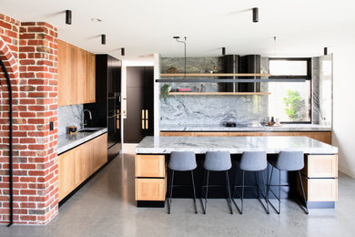 Large industrial galley kitchen pantry in Melbourne with an integrated sink, recessed-panel cabinets, black cabinets, granite benchtops, grey splashback, granite splashback, black appliances, concrete floors, with island, grey floor and grey benchtop.