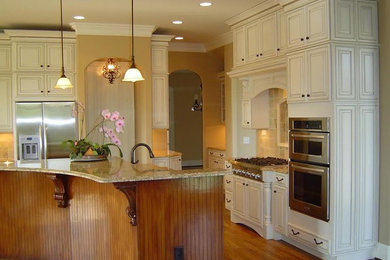 Mid-sized traditional l-shaped eat-in kitchen in San Diego with an undermount sink, raised-panel cabinets, white cabinets, granite benchtops, beige splashback, stone tile splashback, stainless steel appliances, medium hardwood floors, with island and brown floor.