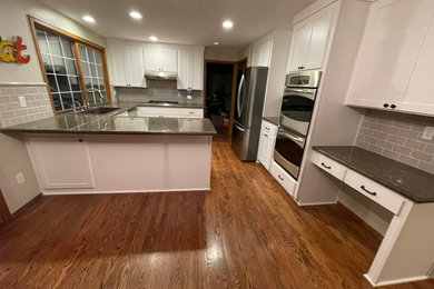 Eat-in kitchen - large transitional u-shaped medium tone wood floor and brown floor eat-in kitchen idea in Tampa with a drop-in sink, shaker cabinets, white cabinets, granite countertops, beige backsplash, subway tile backsplash, stainless steel appliances, a peninsula and brown countertops