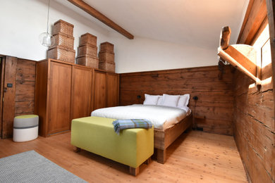 Modelo de dormitorio tipo loft rústico con paredes blancas, suelo beige, vigas vistas y suelo de madera en tonos medios