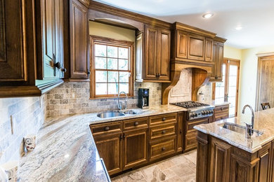 Inspiration for a large traditional u-shaped eat-in kitchen in Kansas City with a double-bowl sink, raised-panel cabinets, medium wood cabinets, granite benchtops, grey splashback, stone tile splashback, stainless steel appliances, travertine floors and with island.