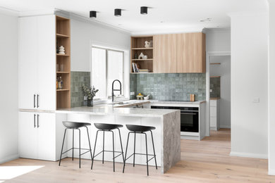 U-shaped kitchen in Melbourne with a double-bowl sink, shaker cabinets, white cabinets, marble benchtops, green splashback, porcelain splashback, black appliances, a peninsula and grey benchtop.