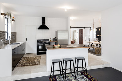 This is an example of a mid-sized scandinavian galley open plan kitchen in Sydney with a double-bowl sink, black cabinets, wood benchtops, white splashback, subway tile splashback, black appliances, limestone floors and with island.