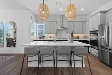 Open concept kitchen - transitional l-shaped medium tone wood floor and brown floor open concept kitchen idea in Phoenix with an undermount sink, shaker cabinets, gray cabinets, gray backsplash, stainless steel appliances, an island and white countertops