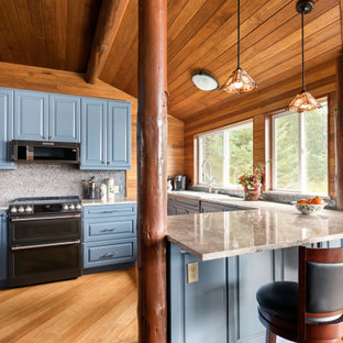 Large country l-shaped open plan kitchen in Seattle with an undermount sink, raised-panel cabinets, blue cabinets, quartz benchtops, blue splashback, glass tile splashback, stainless steel appliances, bamboo floors, a peninsula, brown floor, white benchtop and wood.