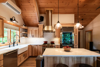 Example of a mid-sized mountain style medium tone wood floor eat-in kitchen design in Portland Maine with a farmhouse sink, raised-panel cabinets, medium tone wood cabinets, granite countertops, white backsplash, ceramic backsplash, stainless steel appliances, an island and white countertops