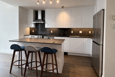 Eat-in kitchen - small modern l-shaped medium tone wood floor and brown floor eat-in kitchen idea in Montreal with a single-bowl sink, flat-panel cabinets, white cabinets, quartz countertops, black backsplash, quartz backsplash, stainless steel appliances, an island and black countertops