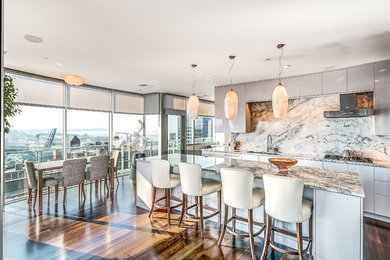 Example of a trendy dark wood floor eat-in kitchen design in Cleveland with an undermount sink, flat-panel cabinets, gray cabinets, multicolored backsplash, stone slab backsplash and an island
