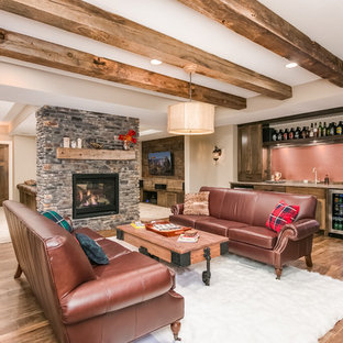 Photo of a medium sized rustic look-out basement in Minneapolis with beige walls, laminate floors, a two-sided fireplace, a stone fireplace surround and brown floors.