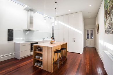 Inspiration for a mid-sized modern single-wall open plan kitchen in Melbourne with an undermount sink, flat-panel cabinets, white cabinets, wood benchtops, glass sheet splashback, stainless steel appliances, dark hardwood floors and with island.