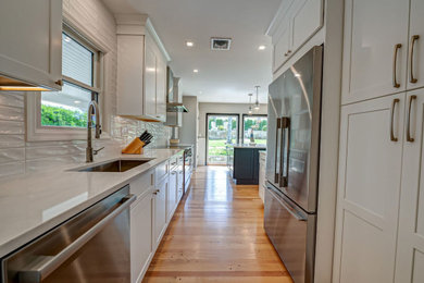 Example of a small transitional galley light wood floor and brown floor eat-in kitchen design in New York with an undermount sink, shaker cabinets, white cabinets, quartz countertops, white backsplash, porcelain backsplash, stainless steel appliances, an island and white countertops