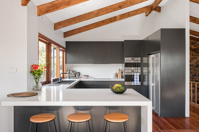 This is an example of a mid-sized contemporary u-shaped open plan kitchen in Sydney with a double-bowl sink, recessed-panel cabinets, black cabinets, quartz benchtops, white splashback, glass sheet splashback, stainless steel appliances, medium hardwood floors, no island, brown floor and white benchtop.