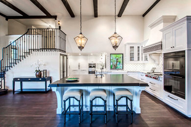 Open concept kitchen - huge mediterranean l-shaped dark wood floor open concept kitchen idea in Santa Barbara with a farmhouse sink, beaded inset cabinets, white cabinets, granite countertops, white backsplash, ceramic backsplash, paneled appliances and an island