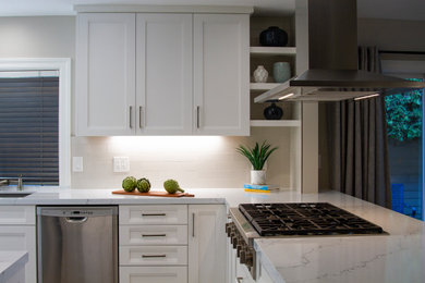 Kitchen photo in Orange County with white cabinets, quartz countertops, stainless steel appliances, a peninsula, white countertops, gray backsplash and subway tile backsplash