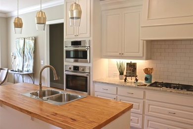 Open concept kitchen - mid-sized traditional l-shaped medium tone wood floor and brown floor open concept kitchen idea in Jackson with a drop-in sink, raised-panel cabinets, white cabinets, wood countertops, white backsplash, subway tile backsplash, stainless steel appliances and an island