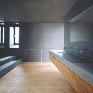 Aménagement d'une très grande salle de bain moderne avec un placard à porte plane, des portes de placard en bois brun, un carrelage gris, des carreaux de béton, un sol en bois clair, un lavabo intégré et un plan de toilette en terrazzo.
