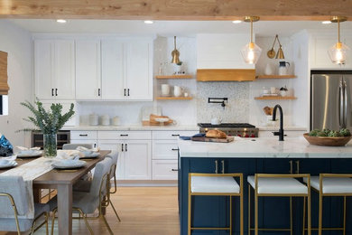 Mid-sized transitional single-wall open plan kitchen in Denver with a farmhouse sink, shaker cabinets, white cabinets, quartz benchtops, white splashback, ceramic splashback, stainless steel appliances, light hardwood floors, with island, beige floor and white benchtop.