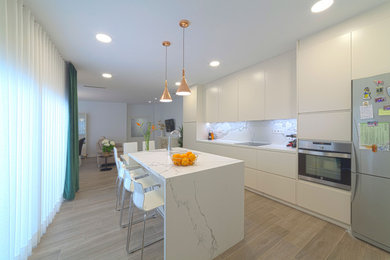 Modelo de cocina lineal contemporánea grande abierta con fregadero bajoencimera, armarios con paneles lisos, puertas de armario beige, encimera de mármol, salpicadero blanco, salpicadero de mármol, electrodomésticos de acero inoxidable, suelo de baldosas de porcelana, una isla, suelo marrón y encimeras blancas