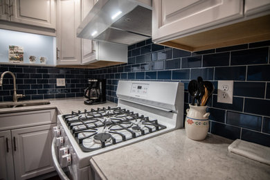 Inspiration for a mid-sized timeless l-shaped dark wood floor and brown floor eat-in kitchen remodel in New York with a double-bowl sink, raised-panel cabinets, white cabinets, quartz countertops, blue backsplash, subway tile backsplash, white appliances, no island and white countertops