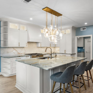 L-shaped white kitchen featuring a large island with a gold-veined slab and a li