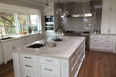 Example of a large transitional u-shaped medium tone wood floor eat-in kitchen design in Sacramento with a single-bowl sink, recessed-panel cabinets, white cabinets, marble countertops, gray backsplash, ceramic backsplash, stainless steel appliances and an island
