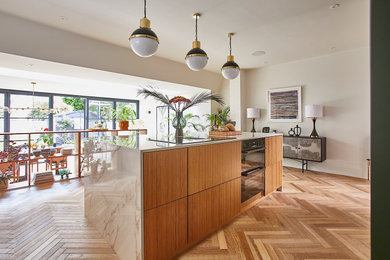 Design ideas for a large contemporary u-shaped kitchen/diner in Sussex with an integrated sink, glass-front cabinets, light wood cabinets, marble worktops, white splashback, porcelain splashback, integrated appliances, medium hardwood flooring, an island, beige floors, black worktops and feature lighting.
