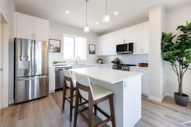 Inspiration for a large modern l-shaped laminate floor eat-in kitchen remodel in Calgary with a drop-in sink, flat-panel cabinets, white backsplash, mosaic tile backsplash, stainless steel appliances, an island and white countertops