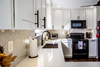 Inspiration for a mid-sized transitional u-shaped vinyl floor, brown floor and vaulted ceiling open concept kitchen remodel in DC Metro with an undermount sink, shaker cabinets, white cabinets, quartz countertops, white backsplash, glass tile backsplash, black appliances, a peninsula and white countertops
