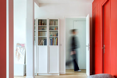 パリにあるお手頃価格の中くらいなコンテンポラリースタイルのおしゃれな玄関ロビー (赤い壁、淡色無垢フローリング、白いドア、ベージュの床) の写真