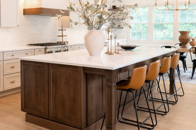 Example of a large transitional u-shaped light wood floor, brown floor and vaulted ceiling eat-in kitchen design in Other with an undermount sink, shaker cabinets, white cabinets, quartz countertops, white backsplash, porcelain backsplash, stainless steel appliances, an island and white countertops