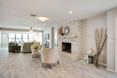Photo of an expansive beach style formal open concept living room in San Diego with grey walls, porcelain floors, a standard fireplace, a brick fireplace surround, no tv and grey floor.