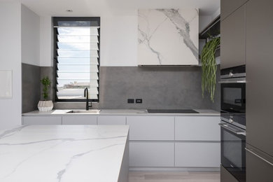 Inspiration for a large contemporary l-shaped open plan kitchen in Perth with grey cabinets, marble benchtops, grey splashback, porcelain splashback, stainless steel appliances, light hardwood floors, with island and white benchtop.