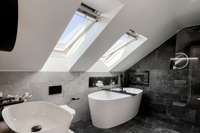 Design ideas for a medium sized contemporary grey and black ensuite half tiled bathroom in West Midlands with flat-panel cabinets, beige cabinets, a freestanding bath, a walk-in shower, a one-piece toilet, grey tiles, ceramic tiles, white walls, ceramic flooring, a console sink, concrete worktops, grey floors, an open shower, grey worktops, feature lighting, a single sink, a floating vanity unit and a vaulted ceiling.