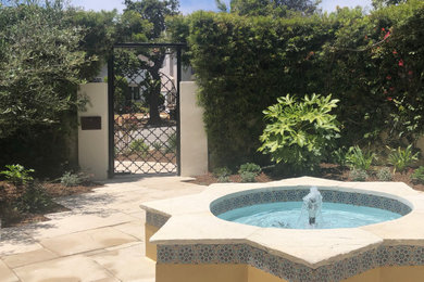Medium sized mediterranean courtyard xeriscape partial sun garden for spring in Los Angeles with a water feature, natural stone paving and a stone fence.