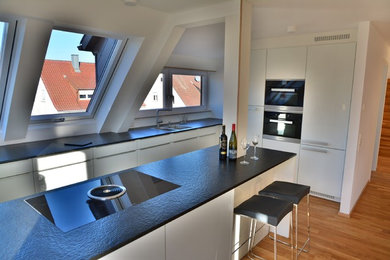 Moderne Wohnküche mit flächenbündigen Schrankfronten, weißen Schränken, Granit-Arbeitsplatte, schwarzen Elektrogeräten und Kücheninsel in Stuttgart