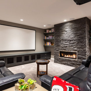 Cette photo montre un grand sous-sol tendance enterré avec salle de jeu, un mur gris, moquette, une cheminée ribbon, un manteau de cheminée en pierre de parement et un sol beige.