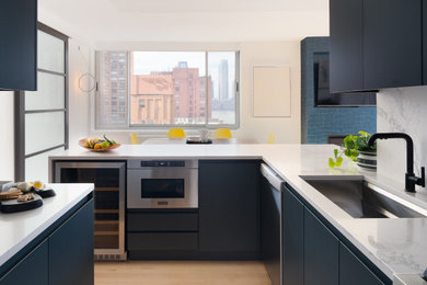 This is an example of a large contemporary u-shaped open plan kitchen in New York with an undermount sink, flat-panel cabinets, blue cabinets, quartz benchtops, white splashback, engineered quartz splashback, stainless steel appliances, light hardwood floors, with island, beige floor and white benchtop.