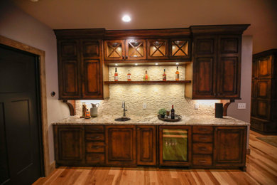 Inspiration for a mid-sized timeless single-wall medium tone wood floor and brown floor wet bar remodel in Other with an undermount sink, raised-panel cabinets, dark wood cabinets, granite countertops, beige backsplash, stone tile backsplash and brown countertops
