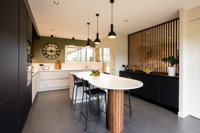 Idées déco pour une grande cuisine blanche et bois contemporaine en L fermée avec un évier encastré, un placard à porte affleurante, des portes de placard noires, plan de travail en marbre, une crédence beige, une crédence en marbre, un électroménager en acier inoxydable, sol en béton ciré, îlot, un sol gris, un plan de travail beige et fenêtre au-dessus de l'évier.