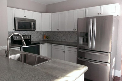 Example of a mid-sized trendy u-shaped dark wood floor eat-in kitchen design in Grand Rapids with a drop-in sink, shaker cabinets, white cabinets, concrete countertops, white backsplash, stone tile backsplash, stainless steel appliances and no island
