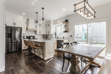 Mid-sized transitional l-shaped dark wood floor and brown floor eat-in kitchen photo in Indianapolis with a farmhouse sink, shaker cabinets, white cabinets, quartz countertops, white backsplash, porcelain backsplash, stainless steel appliances, an island and white countertops