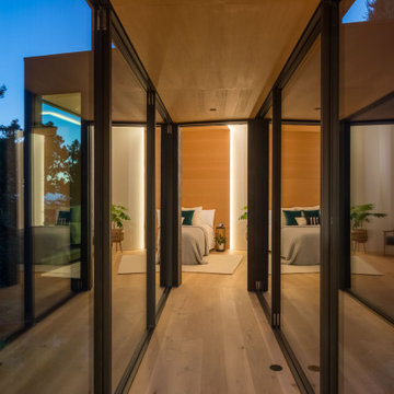 Glass-enclosed hallway connecting main residence to ADU bedroom wing at twilight