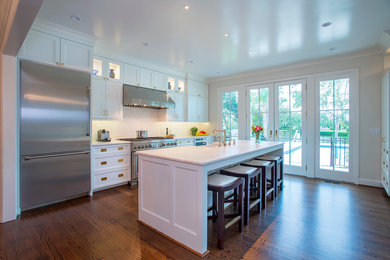 This is an example of a large traditional single-wall eat-in kitchen in Charleston with a farmhouse sink, recessed-panel cabinets, white cabinets, quartz benchtops, white splashback, ceramic splashback, stainless steel appliances, medium hardwood floors, with island and brown floor.