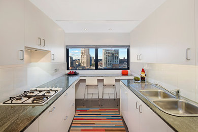 Mid-sized contemporary galley separate kitchen in Sydney with a double-bowl sink, flat-panel cabinets, white cabinets, granite benchtops, white splashback, ceramic splashback, white appliances, ceramic floors, no island and grey floor.