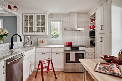 Inspiration for a small transitional light wood floor and brown floor eat-in kitchen remodel in Other with a farmhouse sink, white cabinets, granite countertops, white backsplash, ceramic backsplash, stainless steel appliances and multicolored countertops