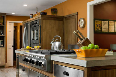 Example of a large urban l-shaped light wood floor and beige floor enclosed kitchen design in Portland Maine with a farmhouse sink, flat-panel cabinets, stainless steel cabinets, concrete countertops, stainless steel appliances and an island