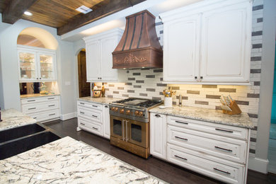 Open concept kitchen - huge traditional dark wood floor open concept kitchen idea in Houston with a farmhouse sink, raised-panel cabinets, white cabinets, granite countertops, multicolored backsplash, stone tile backsplash, stainless steel appliances and an island