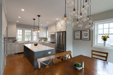 Photo of a large traditional eat-in kitchen in DC Metro with white cabinets, grey splashback, stainless steel appliances, medium hardwood floors, with island and white benchtop.