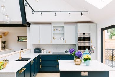 Design ideas for a mid-sized contemporary l-shaped kitchen in London with a double-bowl sink, marble benchtops, white splashback, marble splashback, stainless steel appliances, with island and beige floor.